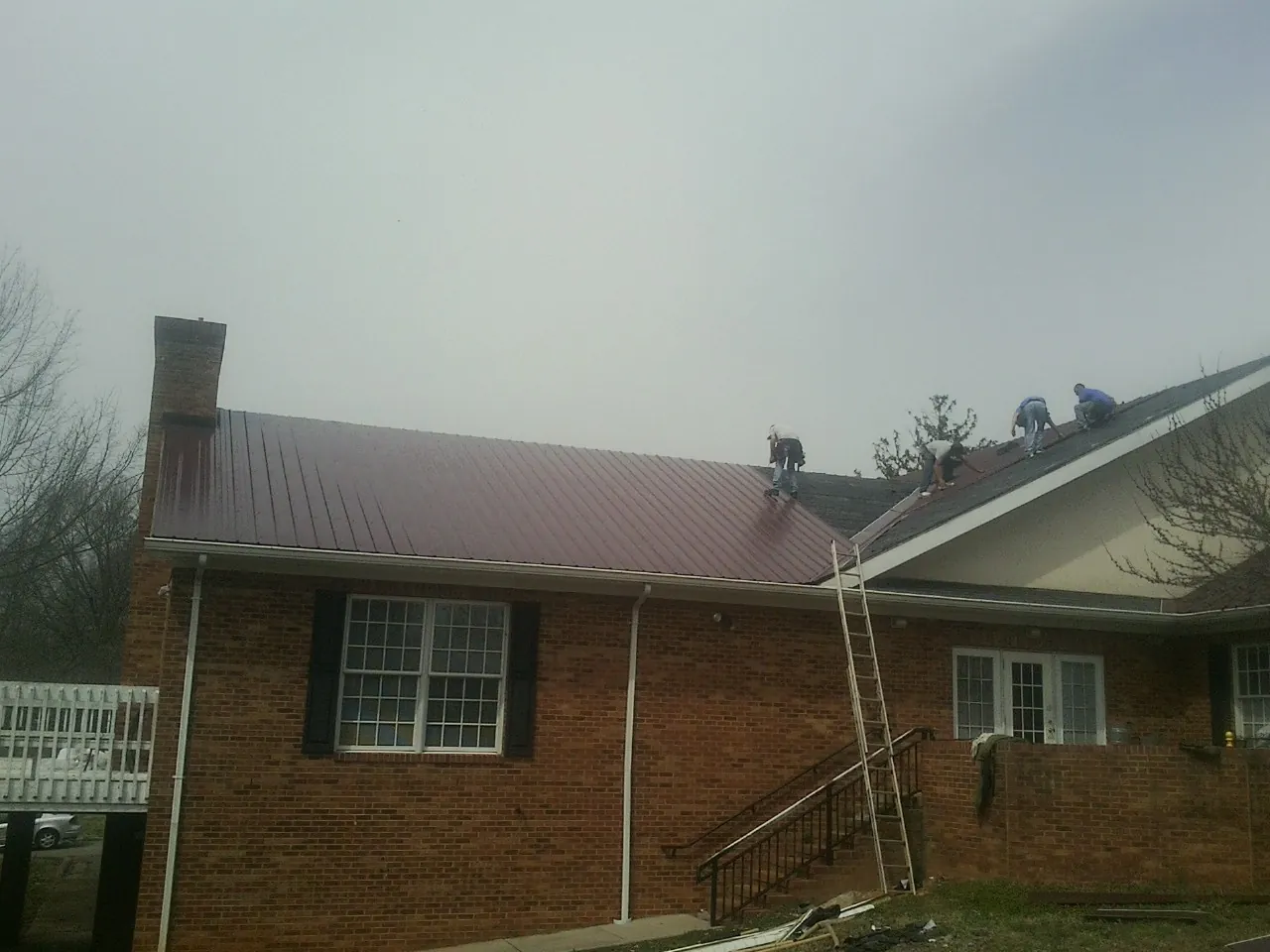Crew setting red metal roofing panels on a brick home in Norman Park
