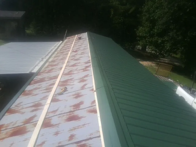Old rusted panels beside newly installed green metal roofing — Wind Damage Roof Repair by Roofing Brothers in Norman Park