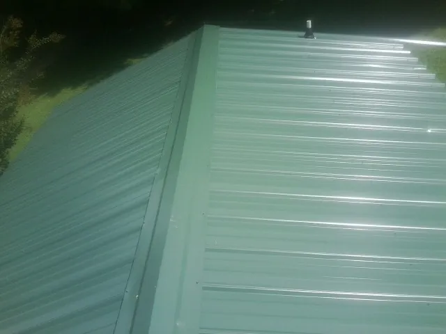 New green metal panels meeting at the ridge of a roof — Flat Roof Repair work by our crew in Norman Park
