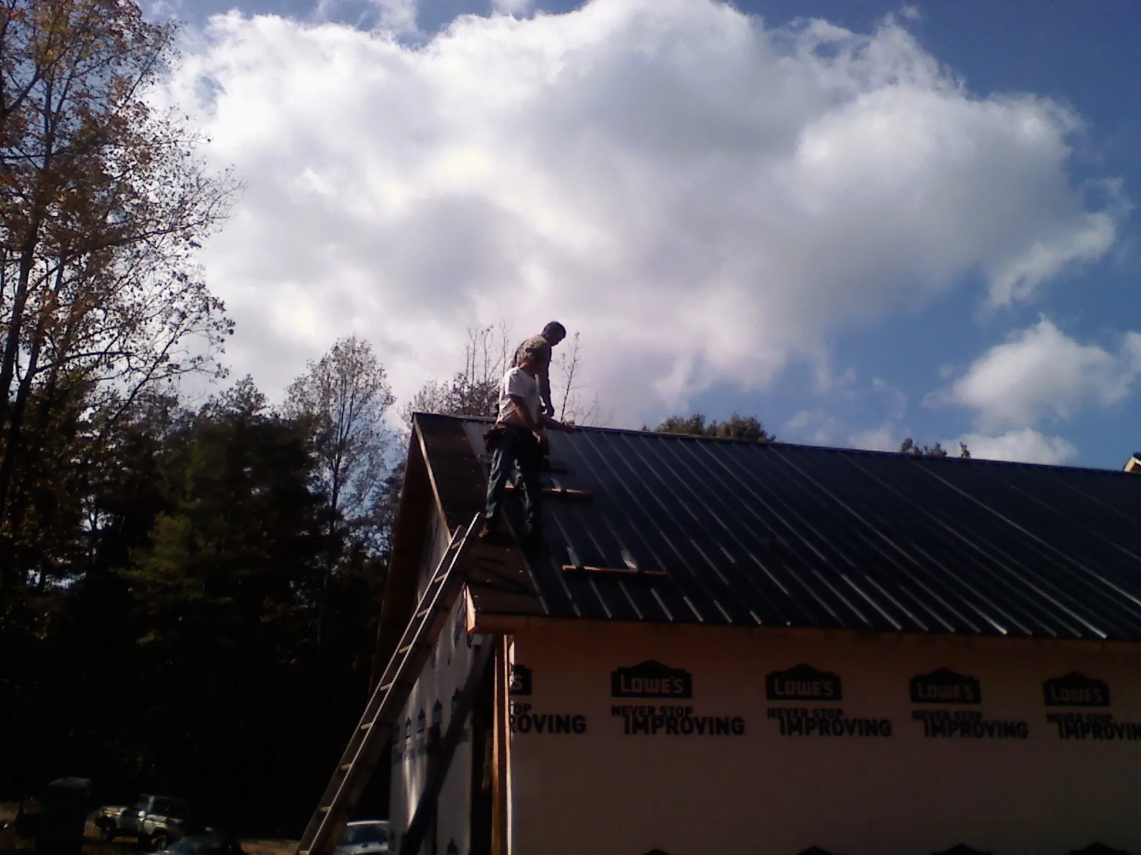 Roofer fastening dark metal panels high against a cloudy sky, from a Roof Inspection job in Norman Park