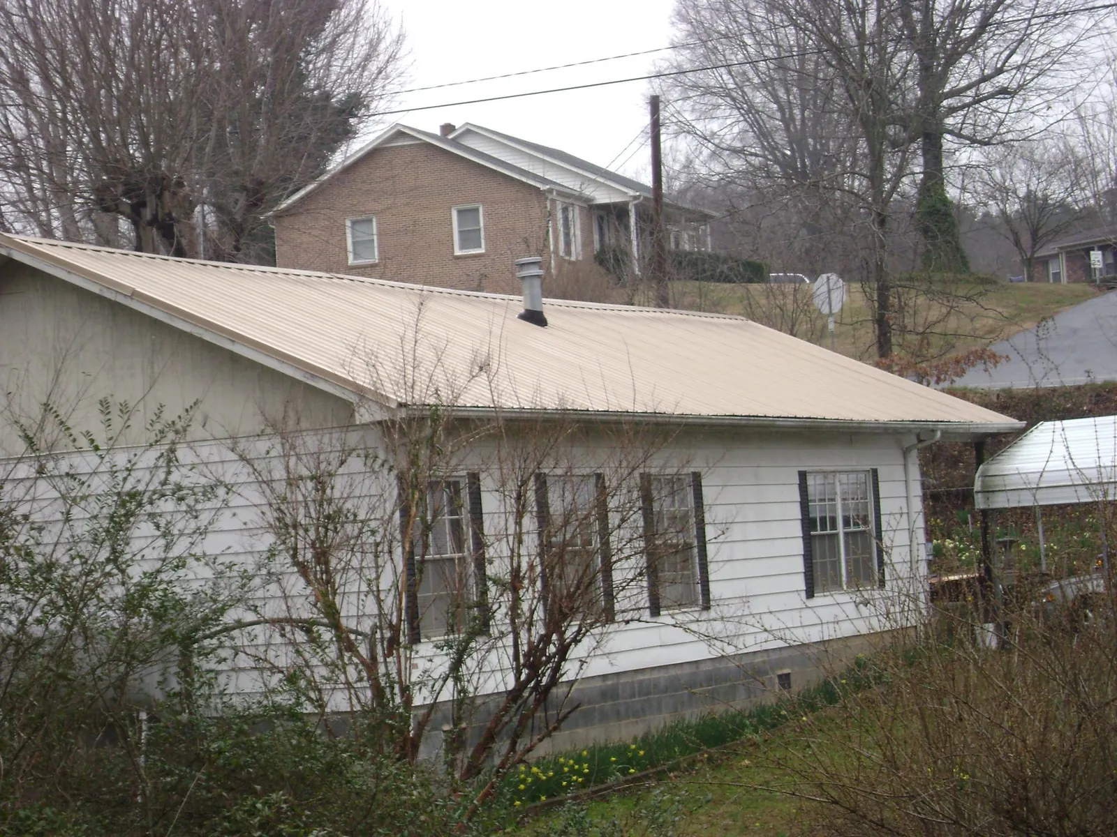Tan metal roof on a white sided house set into a hillside — Commercial Roofing by Roofing Brothers in Norman Park