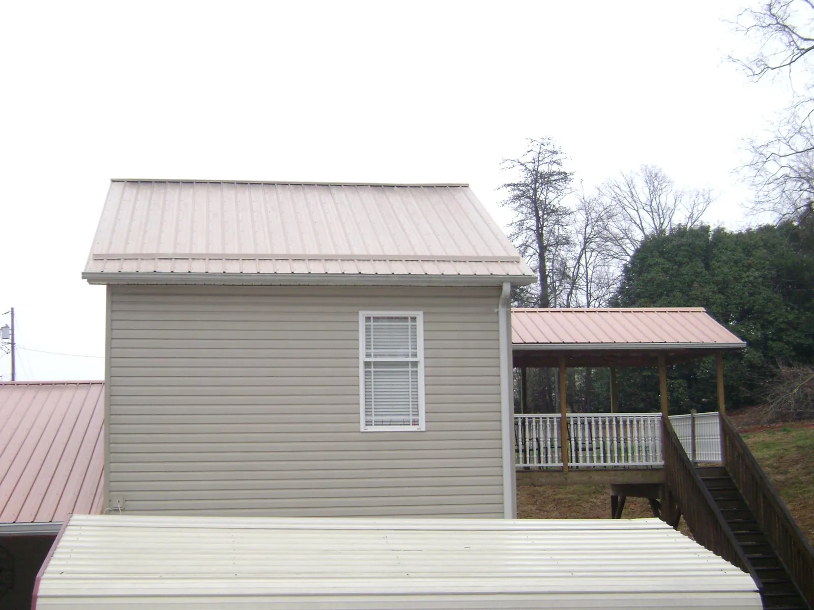 Tan metal roofs on a two story addition and attached porch, from a Roof Replacement job in Norman Park